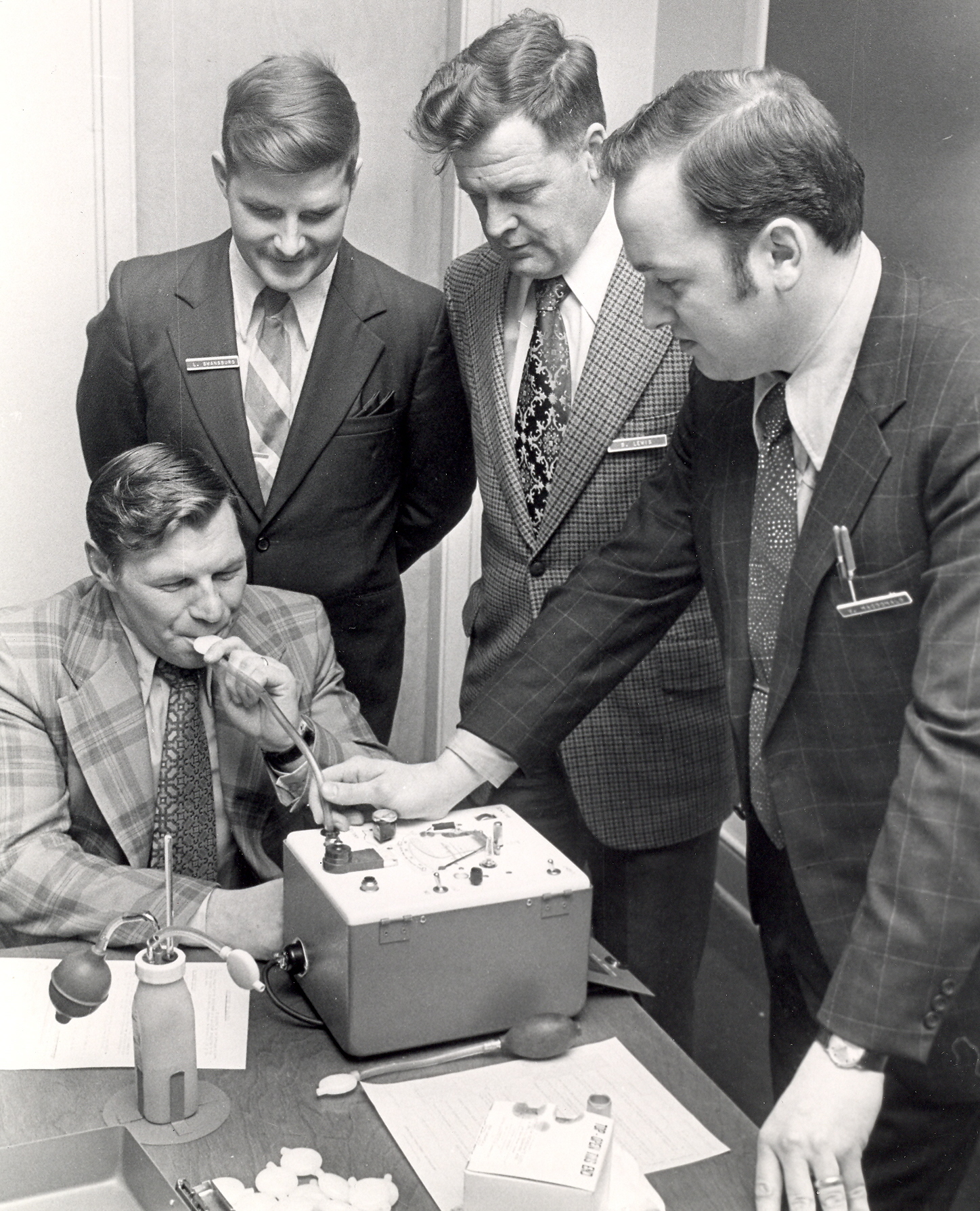 Black-and-white photo of police officers observing a breathalyser demonstration, 1969