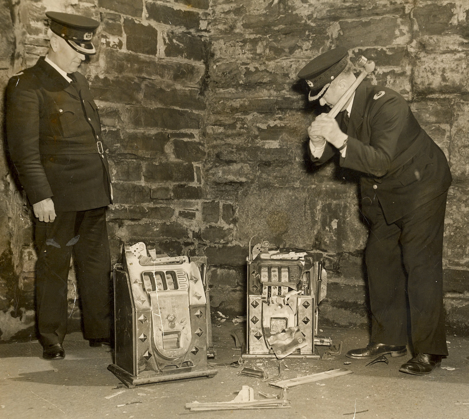 Black and white photograph of policemen smashing a slot machine with a hammer.