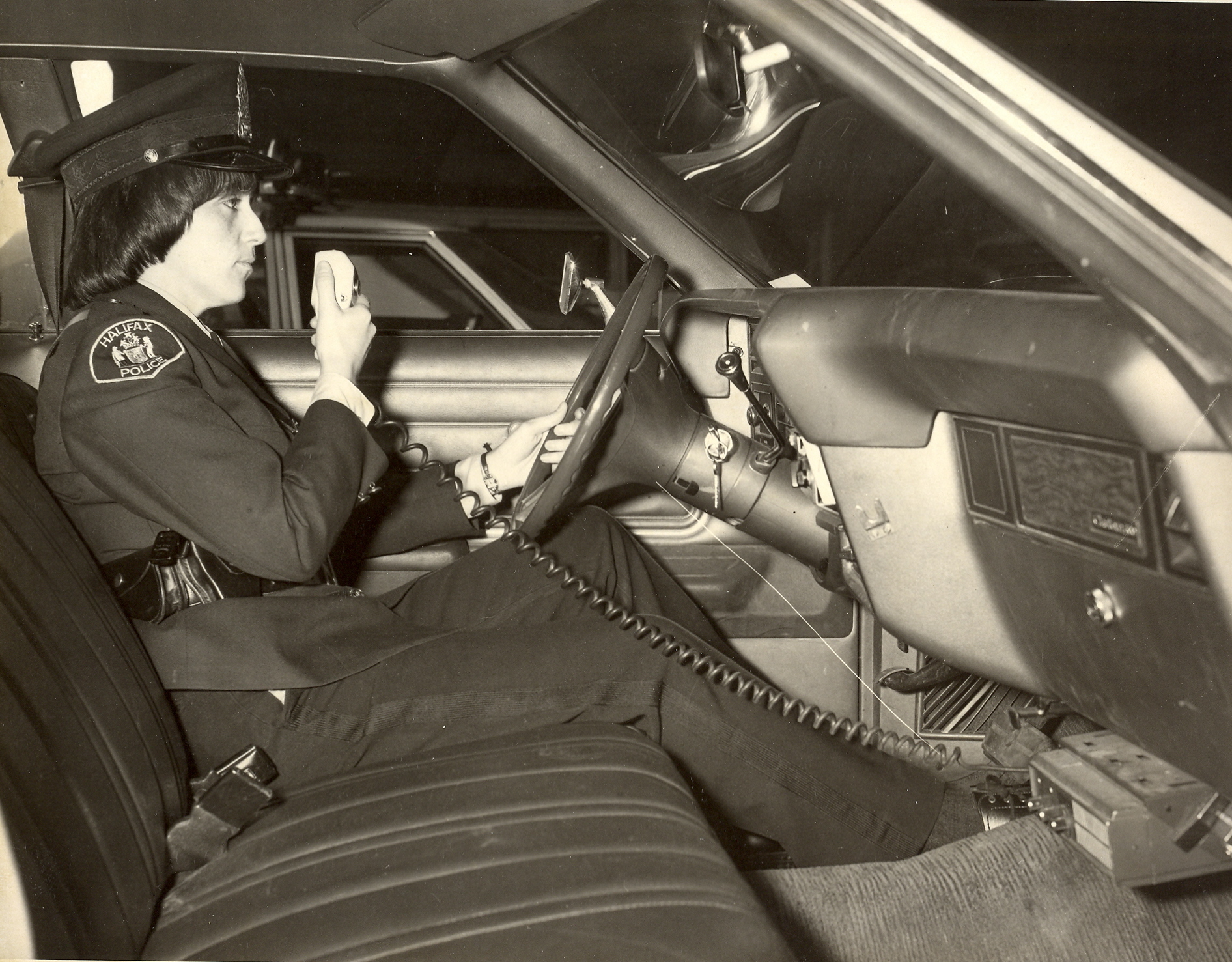 Black and white photo of female officer sitting in car talking on radio