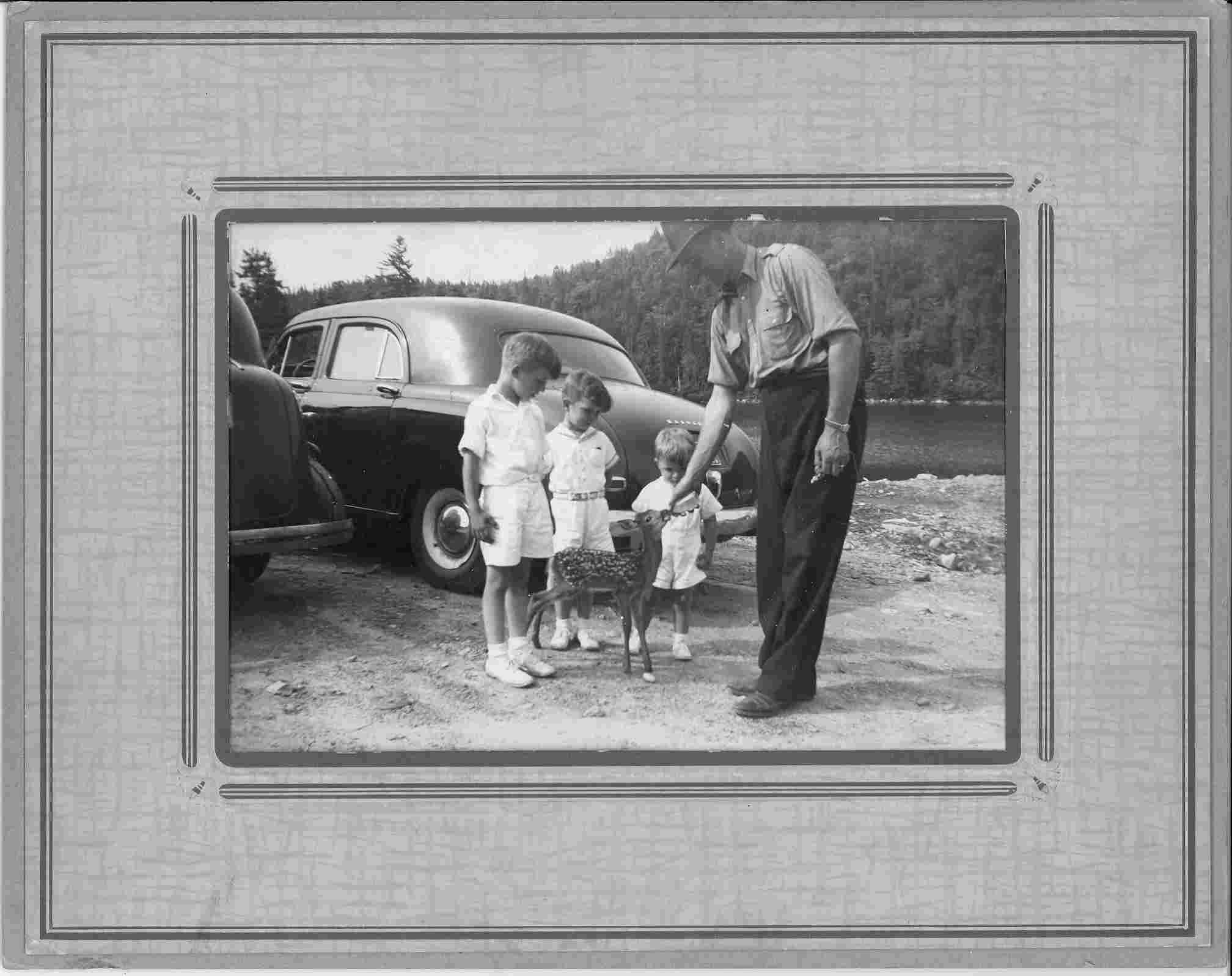 Black and white photo of a police office and three boys feeding a deer.