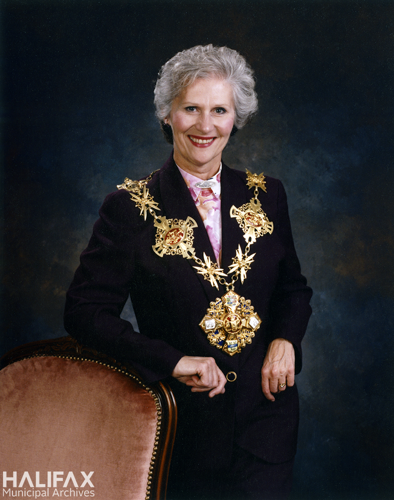 COlour photograph of a woman stadning beside a chair wearing the Mayor's chain of office for the City of Halifax