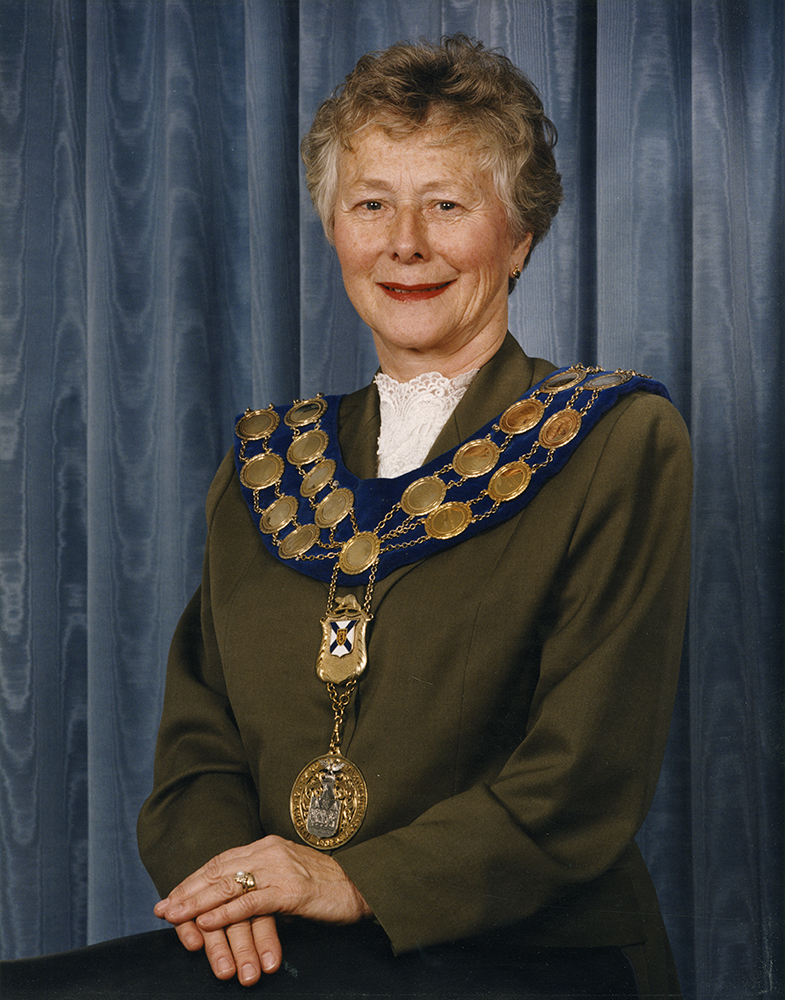 Colour photograph of a woman standing beside a chair wearing the mayor's chain of office for the City of Dartmouth