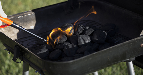 Close up image of a person using a propane barbecue lighter to light charcoal briquettes