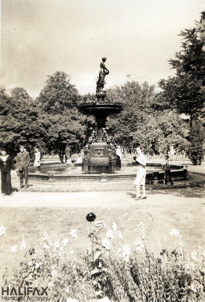 Black and white image of a fountain with a young woman, a small child, and two military servicemen nearby