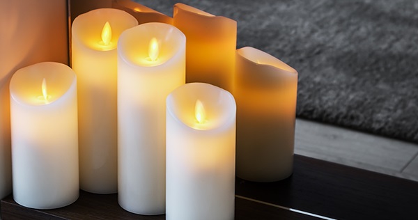 Close up image of seven lit LED candles of varying heights on a table spaced closely together.