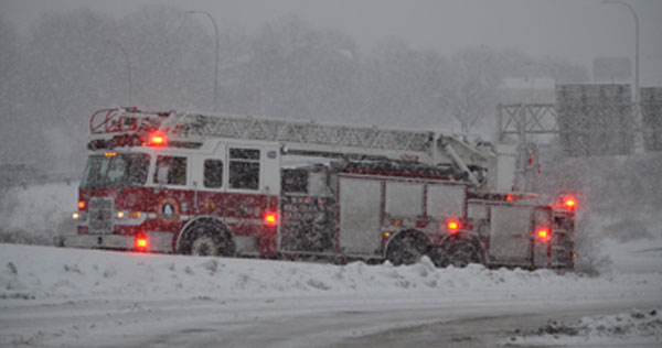 Image of a Fire Truck stopped on the side of the road with lights flashing during a winter storm.