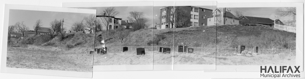 Composite black and white panorama of a cemetary with buildings in the background.