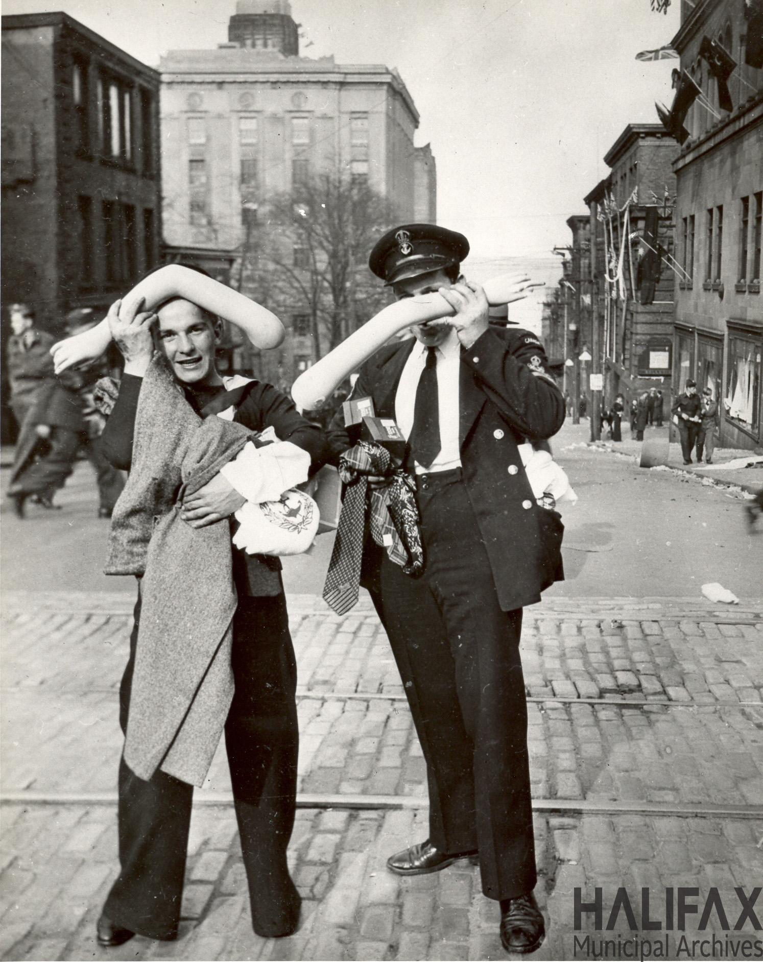 Black and white photographs of two men in uniform holding parts of a mannequin and with their pockets stuffed with stolen merchandise