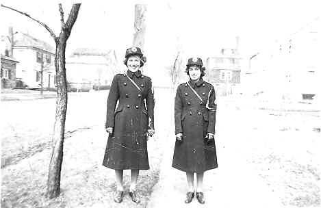 Black & white photo of Keshen sisters standing in uniform in front of houses.
