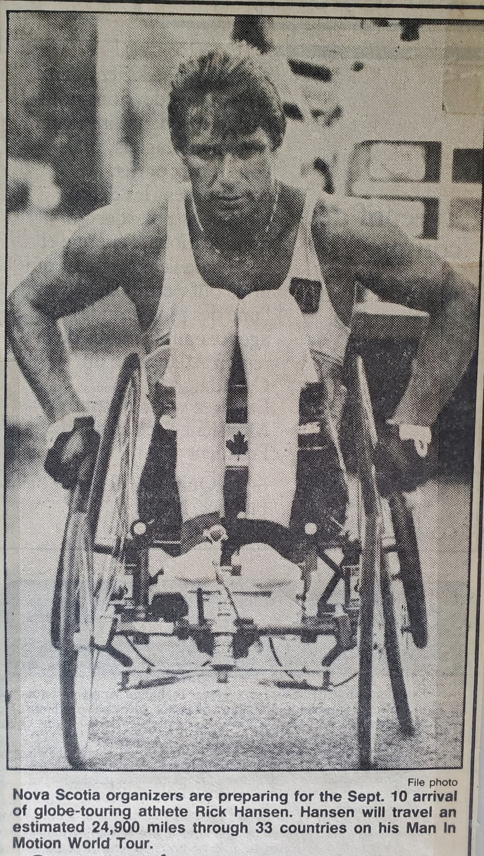 A newspaper clipping of Rick Hansen, wheeling towards the camera. Caption reads: Nova Scotia organizers are preparing for the Sept. 10 arrival of globe-touring athlete Rick Hansen. Hansen will travel an estimated 24,900 miles through 33 countries on his Man in Motion World Tour.