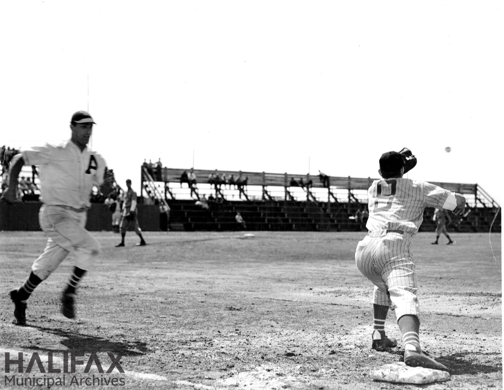 Black and white photograph of a runner approaching first base while the baseman reaches for the incoming throw
