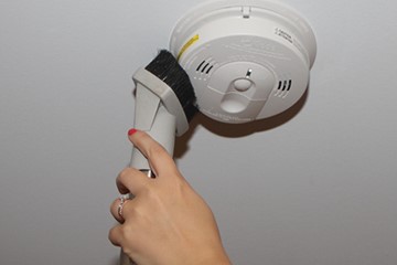 Image of brush cleaning a smoke alarm on ceiling