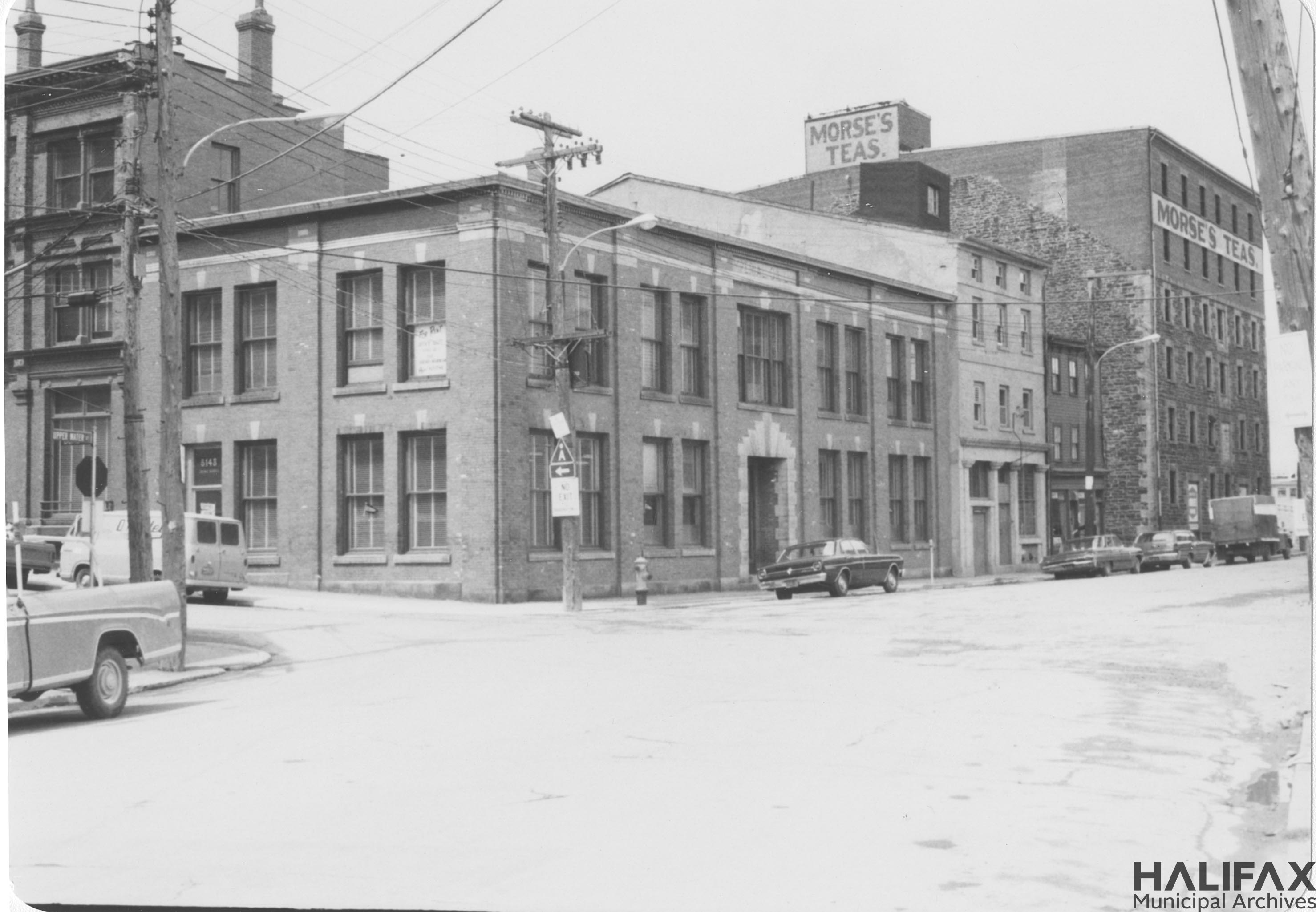 Black and white photo of a row of buildings on a street corner; the Morse's Tea building is on the far right.