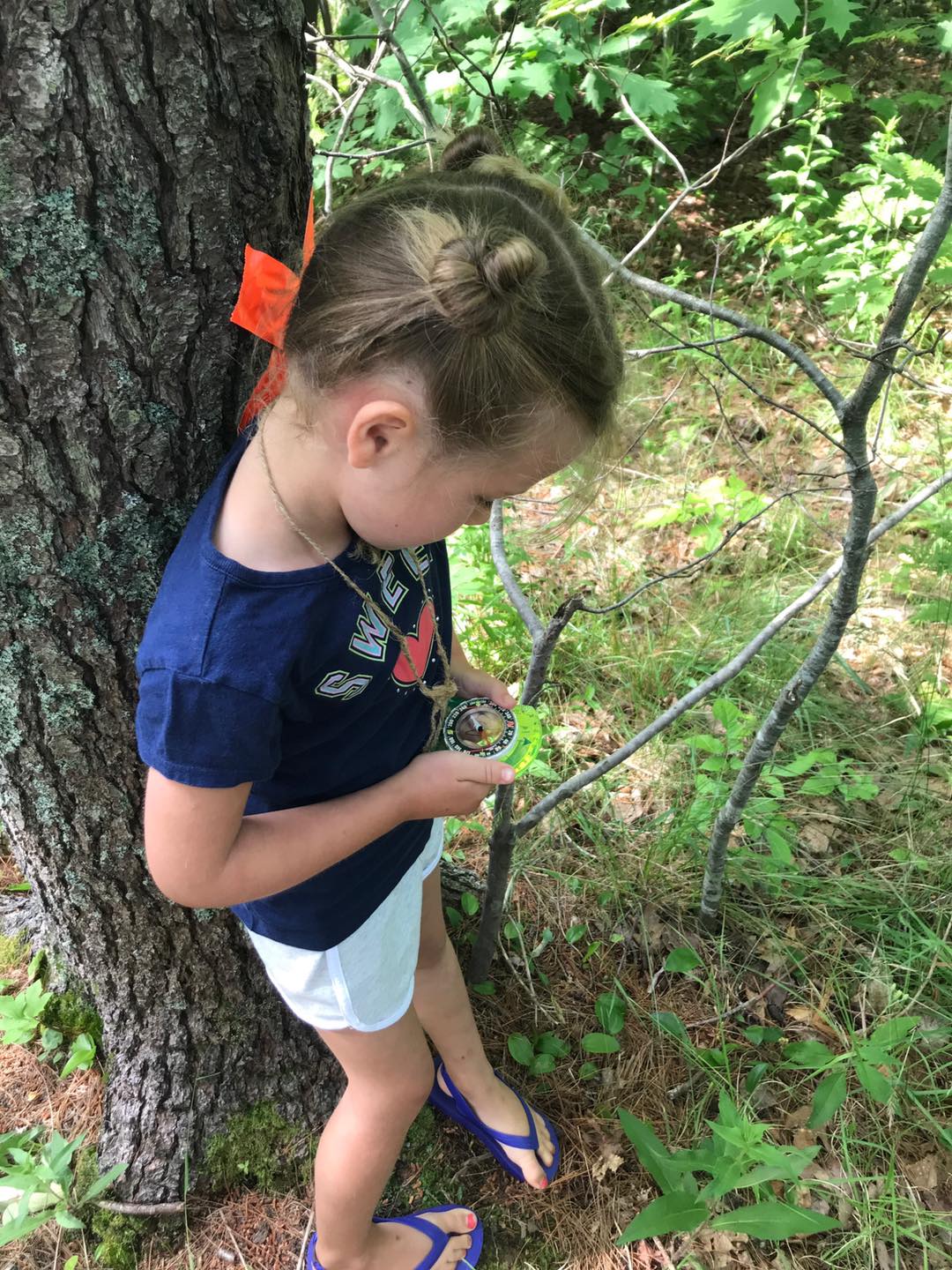 A child looks at a compass in the woods