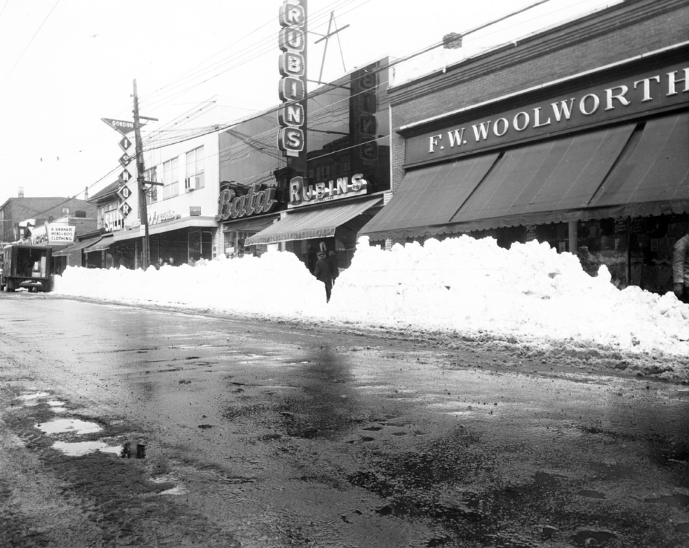 Black and white photo showing shops on a street in winter time