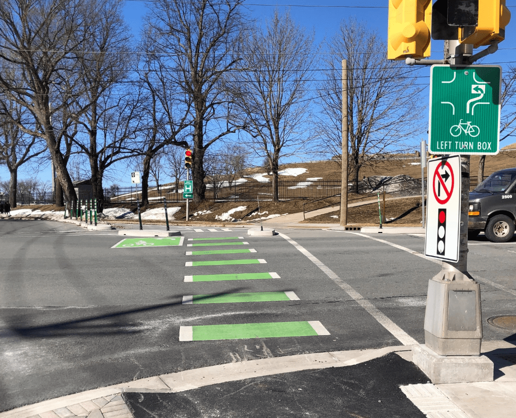 A photo of the South Park Street and Sackville Street intersection, featuring the green paint marking a two-stage left turn box for cyclists. There is a signpost on the right with a white no turn on right sign and a green left turn box sign.