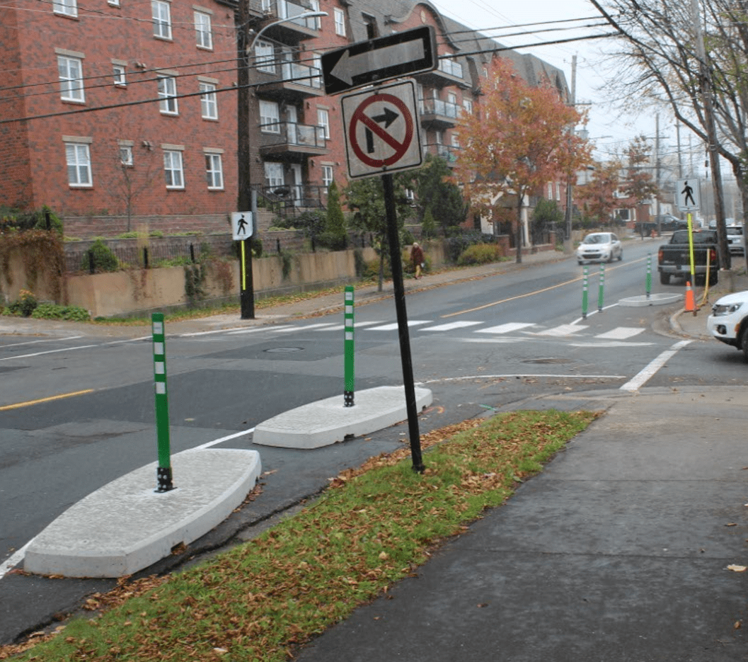 A photo of a street that is being temporarily narrowed using oblong slabs of concrete with green flexible bollards on top of them for visibility.