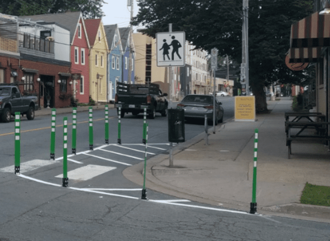 Photo of the corner of the Agricola and Charles Street intersection where the corner of the curb is extended using painted white lines and flexible green bollards.