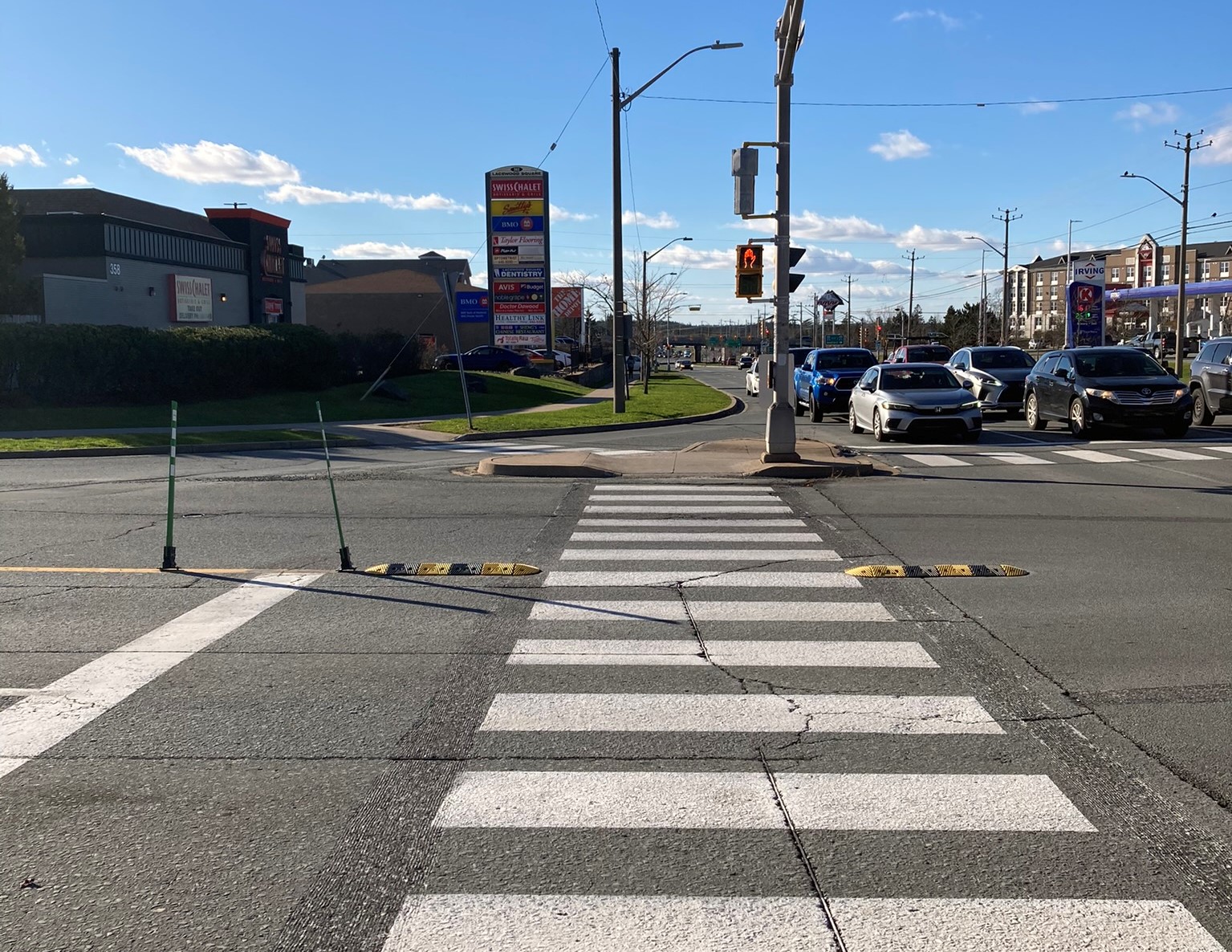 Looking straight across a crosswalk at an intersection, small speed bumps to calm left turns are shown on both sides of the crosswalk