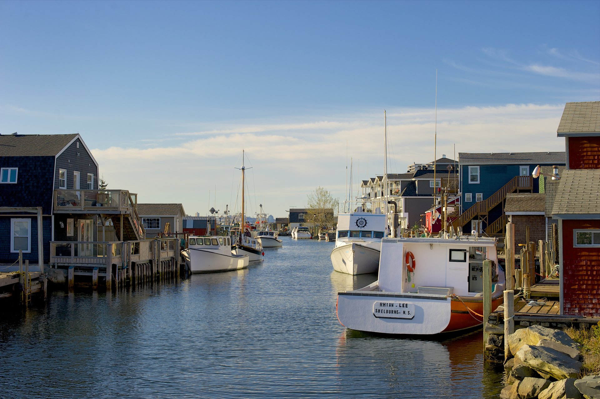 A harbour in Eastern Shore on a sunny day. There are wharves and buildings along the water and white sailboats docked along the boardwalk.