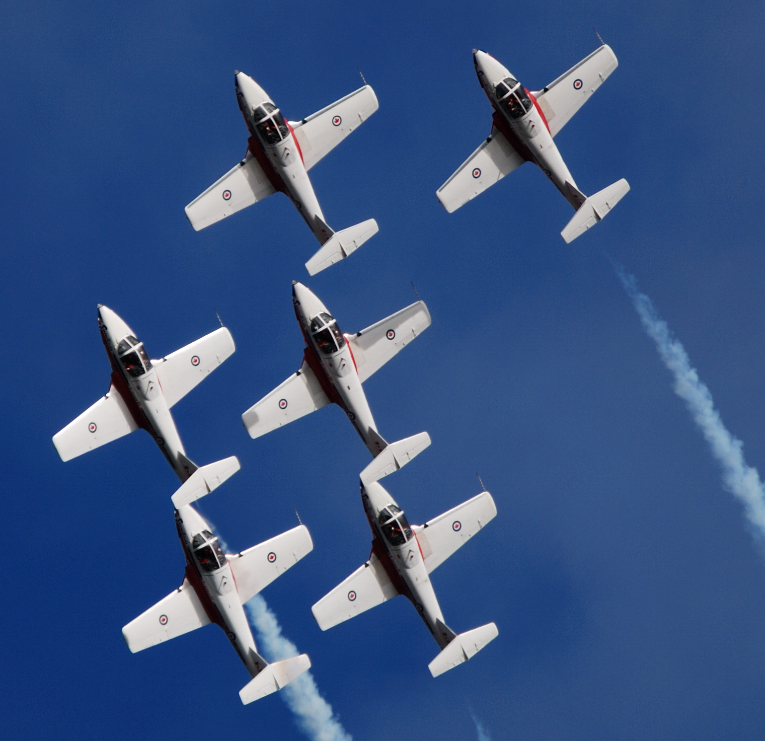 Six military aircraft perform an aerial display against a dark blue sky.