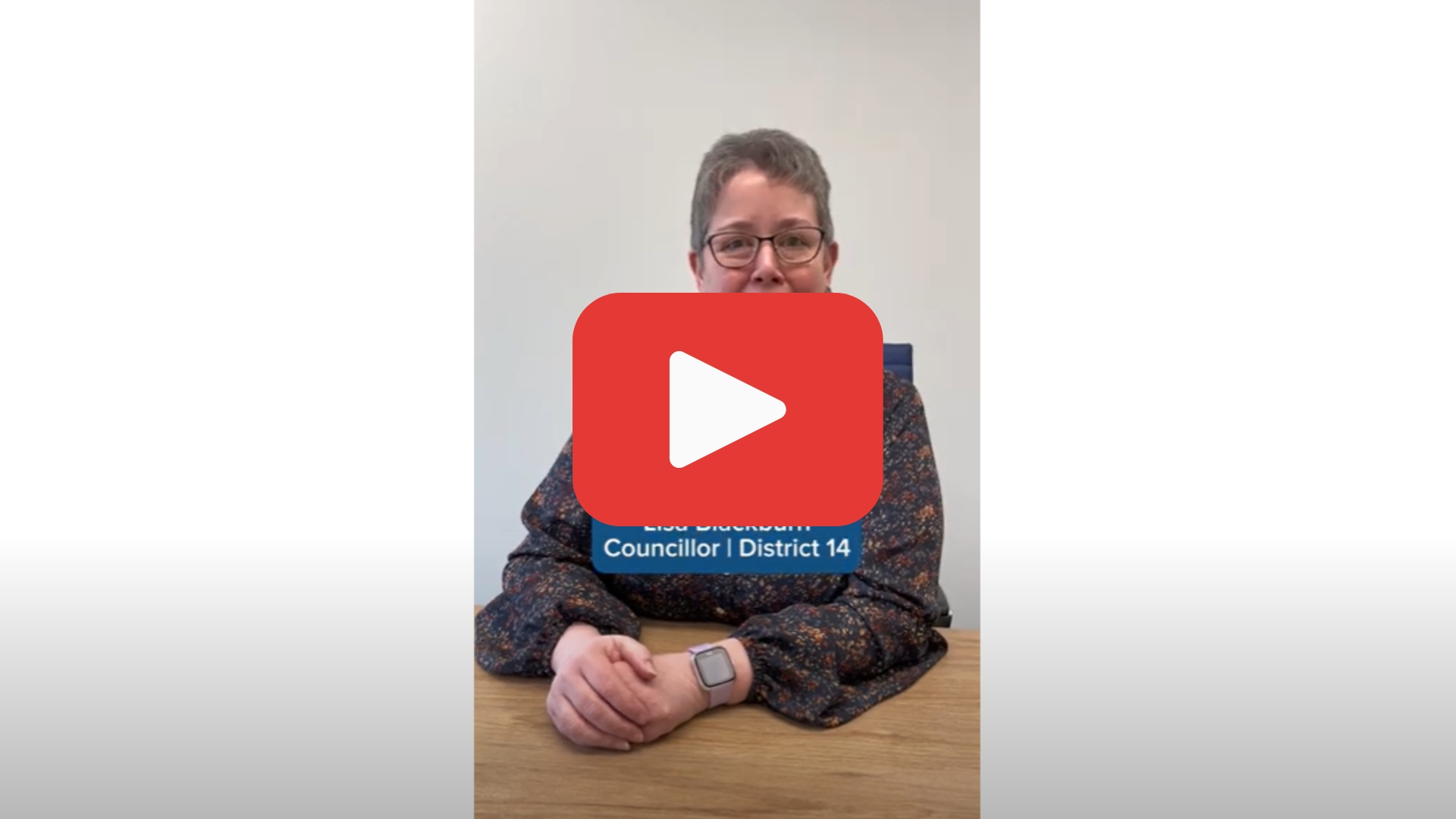Video screenshot of Councillor Lisa Blackburn sitting at a desk with a YouTube "play button" superimposed on her.
