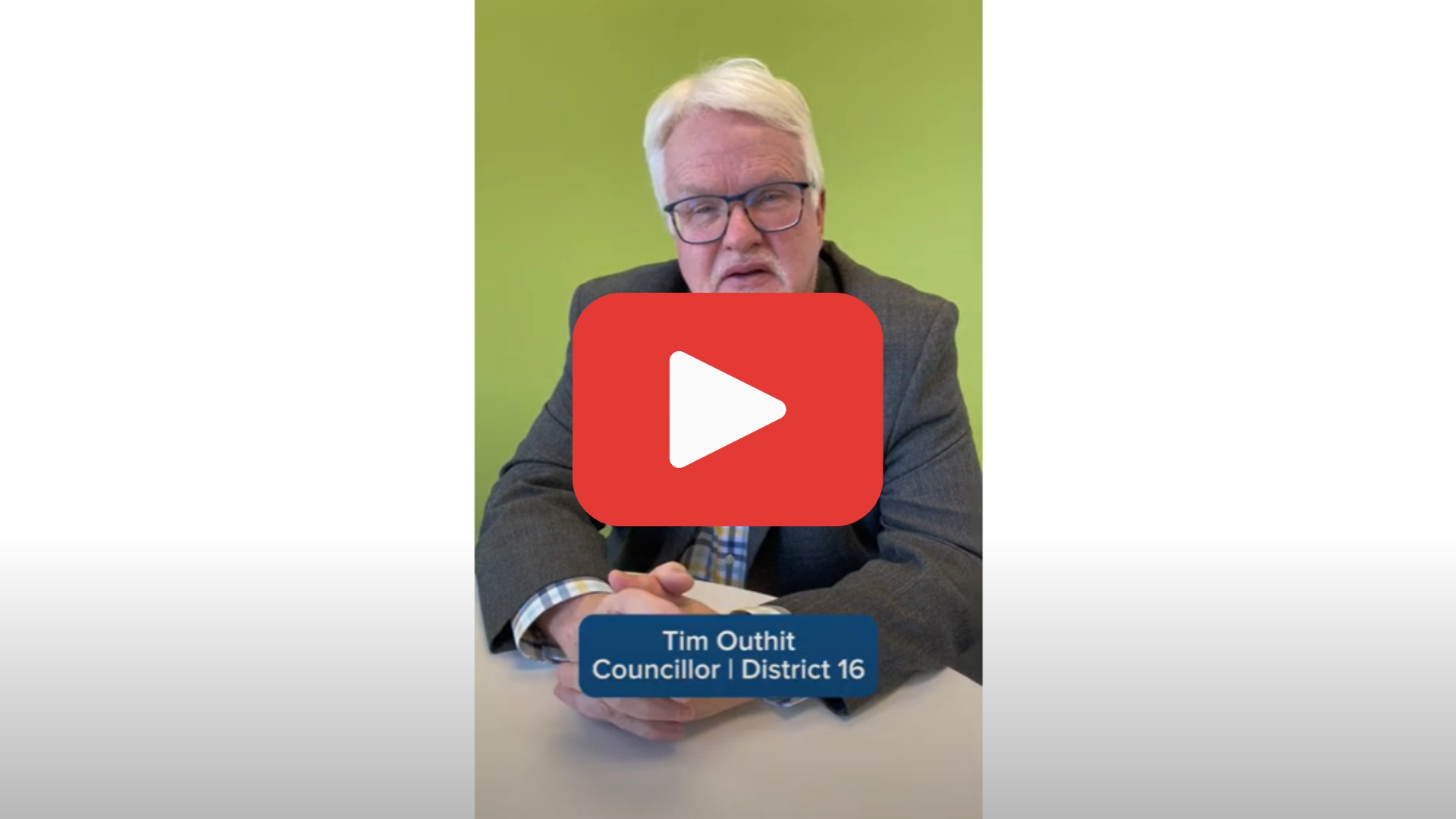 Video screenshot of Councillor Tim Outhit sitting at a desk with a YouTube "play button" superimposed on him.