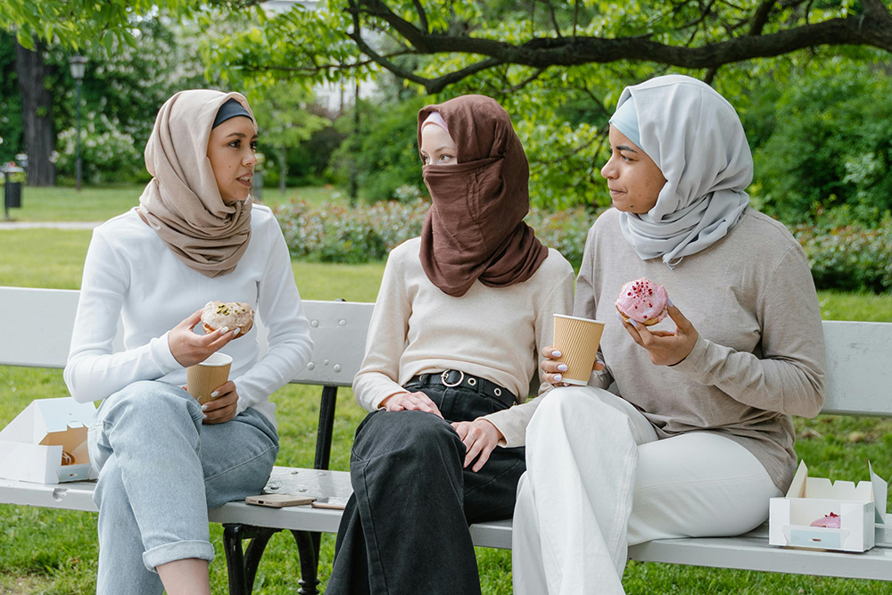 Three women wearing hijabs in various colours sitting on a bench.