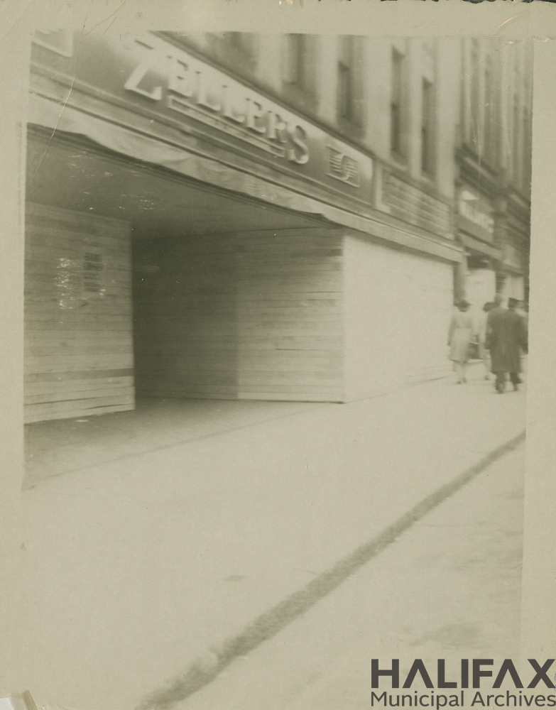 Black and white photo of a street and Zeller's sign with boarded up windows and doors.