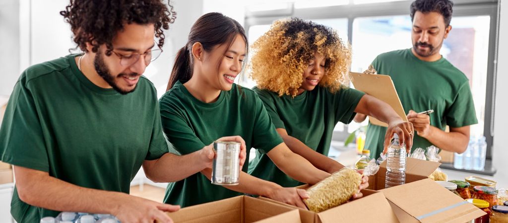 Four volunteers in green t-shirts, packing food donations at a local non-profit