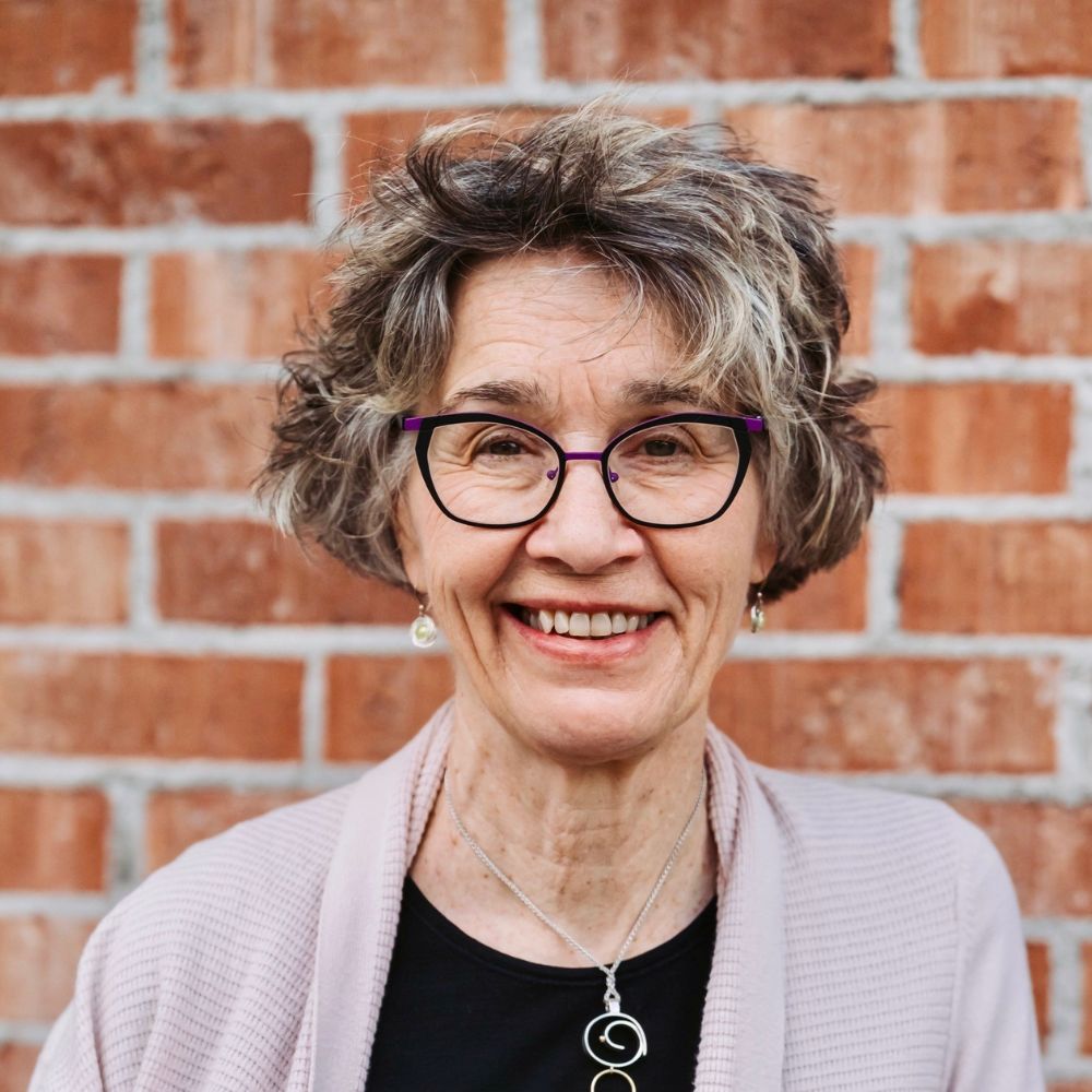 Woman wearing glasses, shirt and cardigan smiling at the camera.