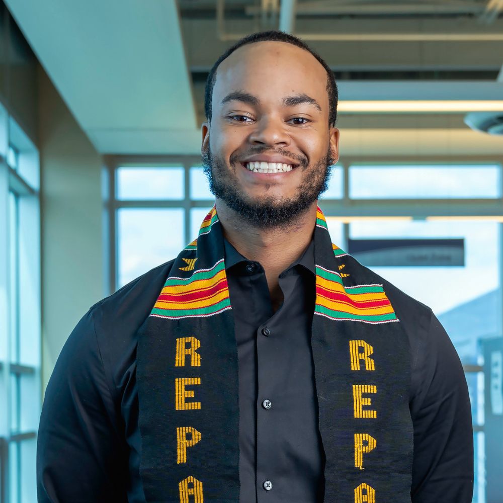 Man wearing a kente scarf smiling at the camera.