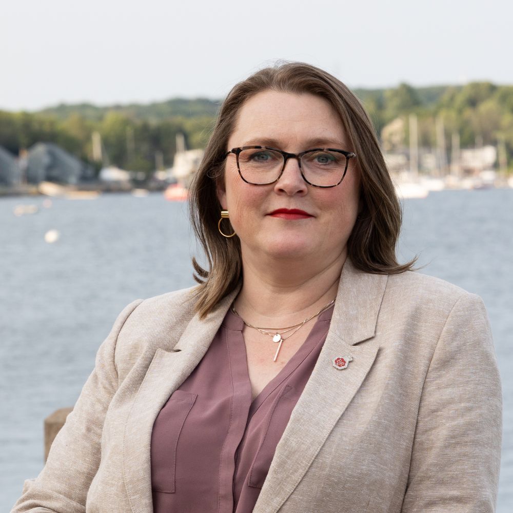 Woman with glasses standing in front of water smiling.