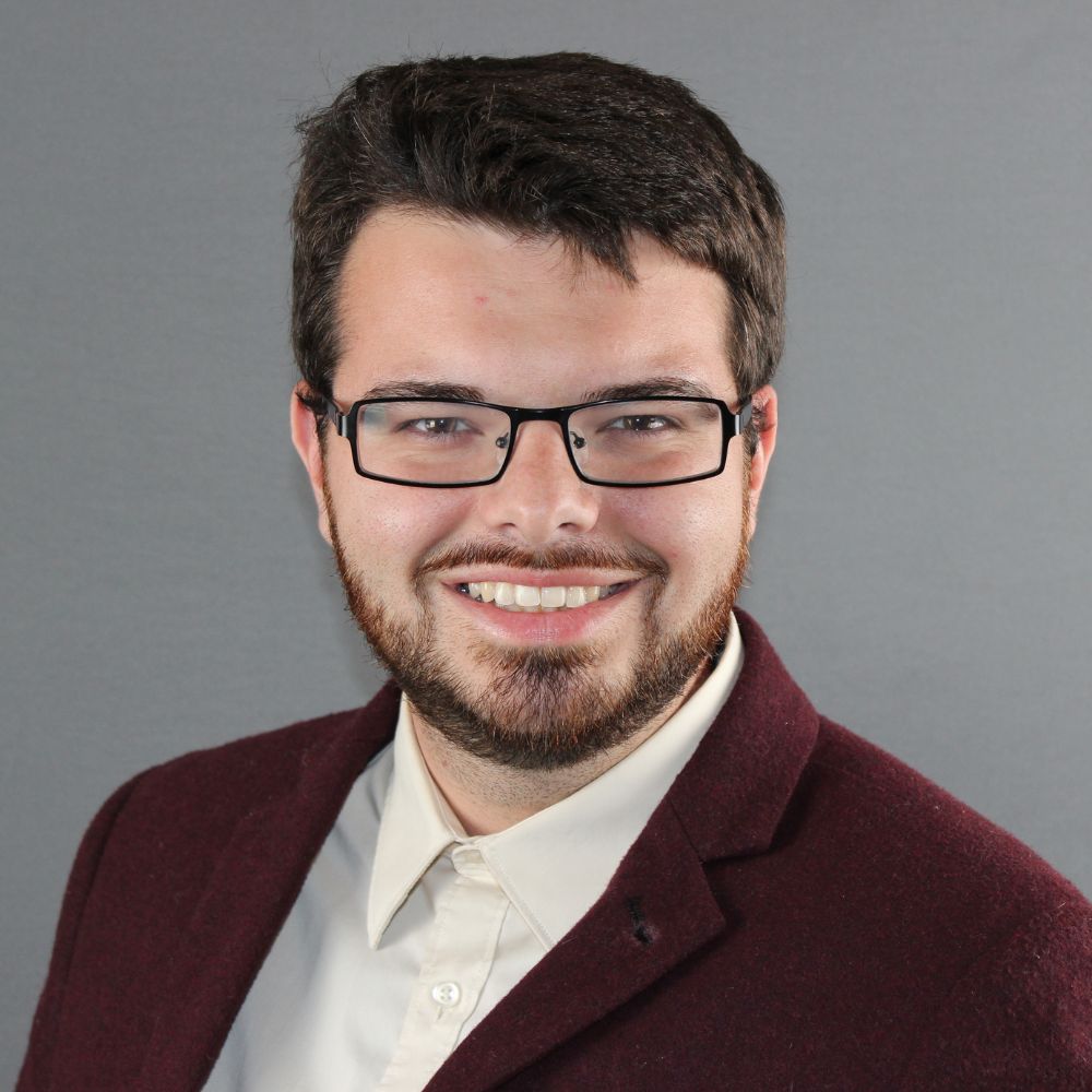 Man wearing a button-up shirt and suit jacket smiling at the camera.