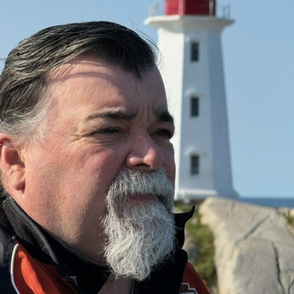 Man standing in front of a lighthouse looking off into the distance.