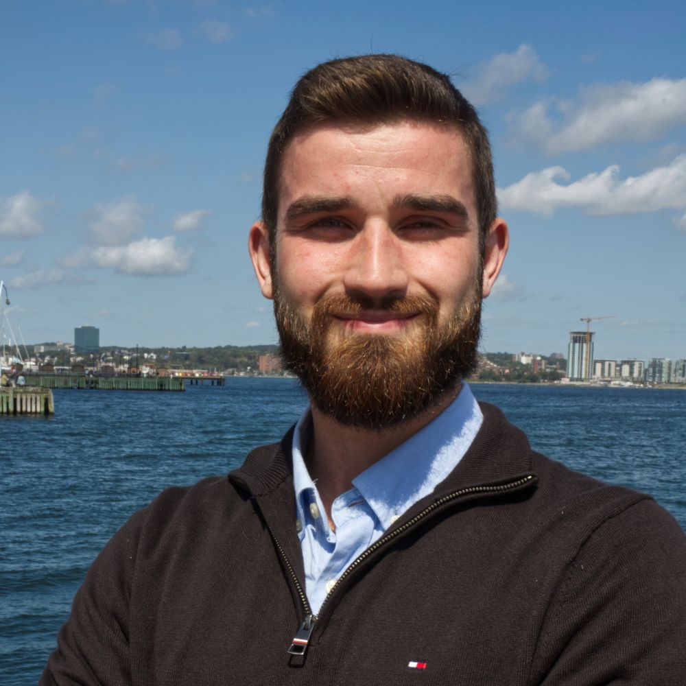 Man standing in front of the Halifax Harbour smiling at the camera.