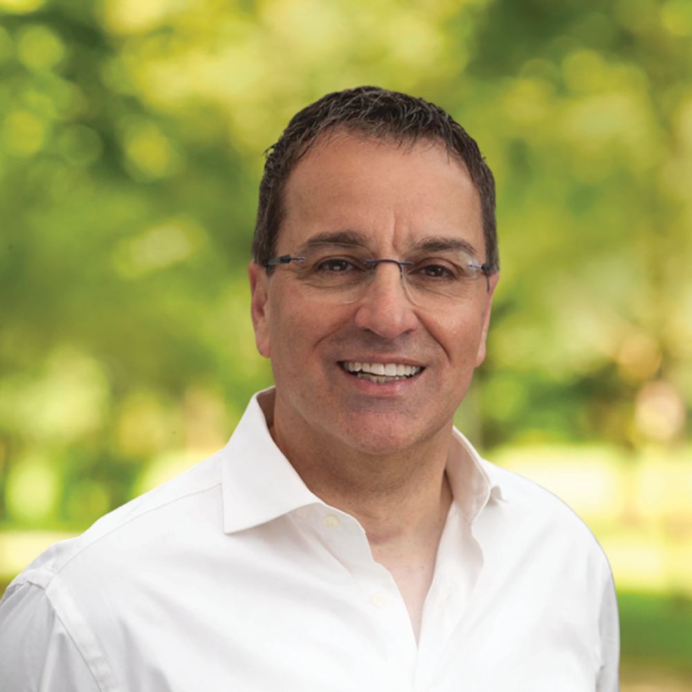 Man with glasses standing outside smiling at camera.