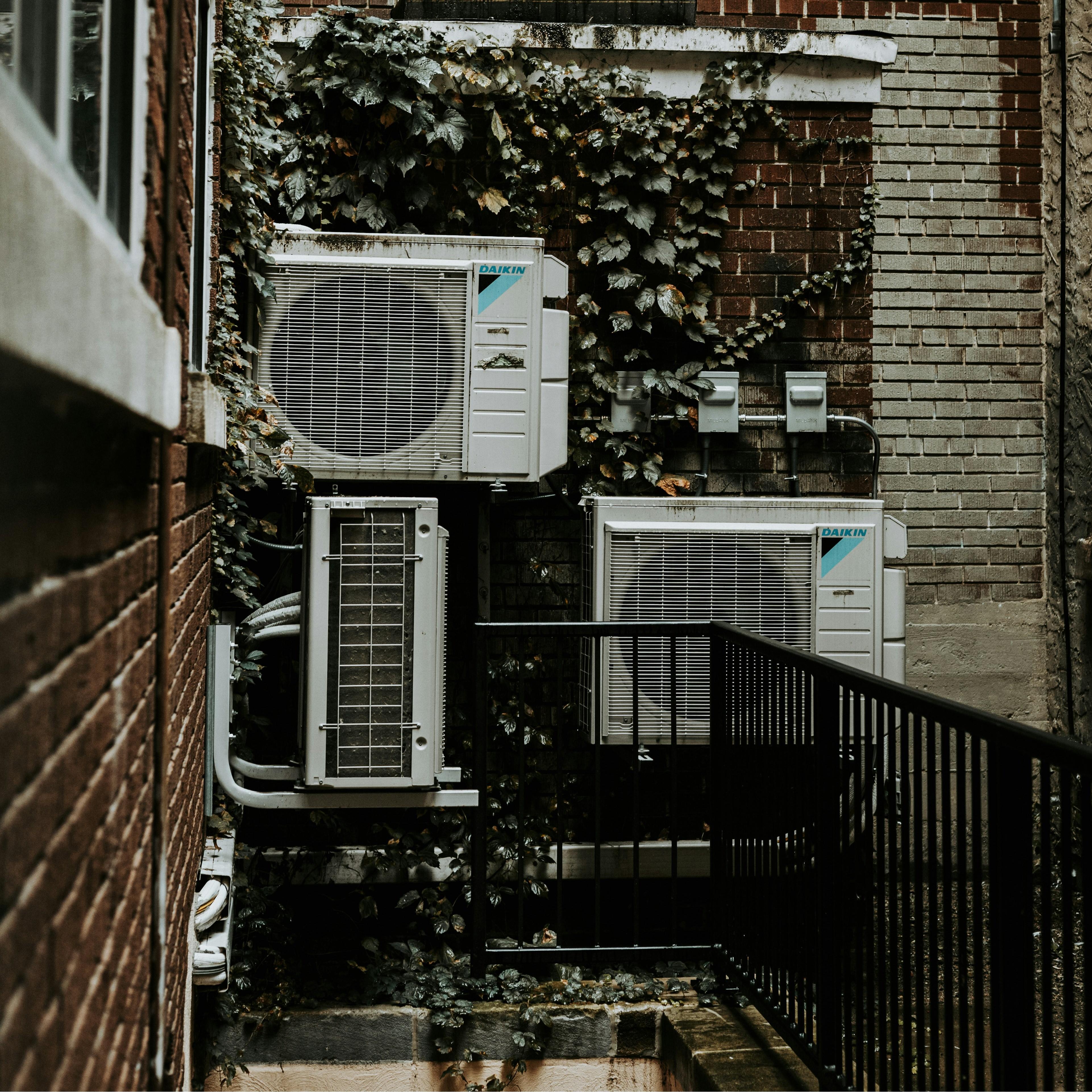 Exterior corner of an apartment building with several appliance attached to the wall.