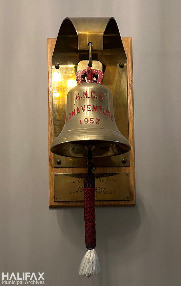 colour photo of bell hanging from wooden plaque with tasselled ringer