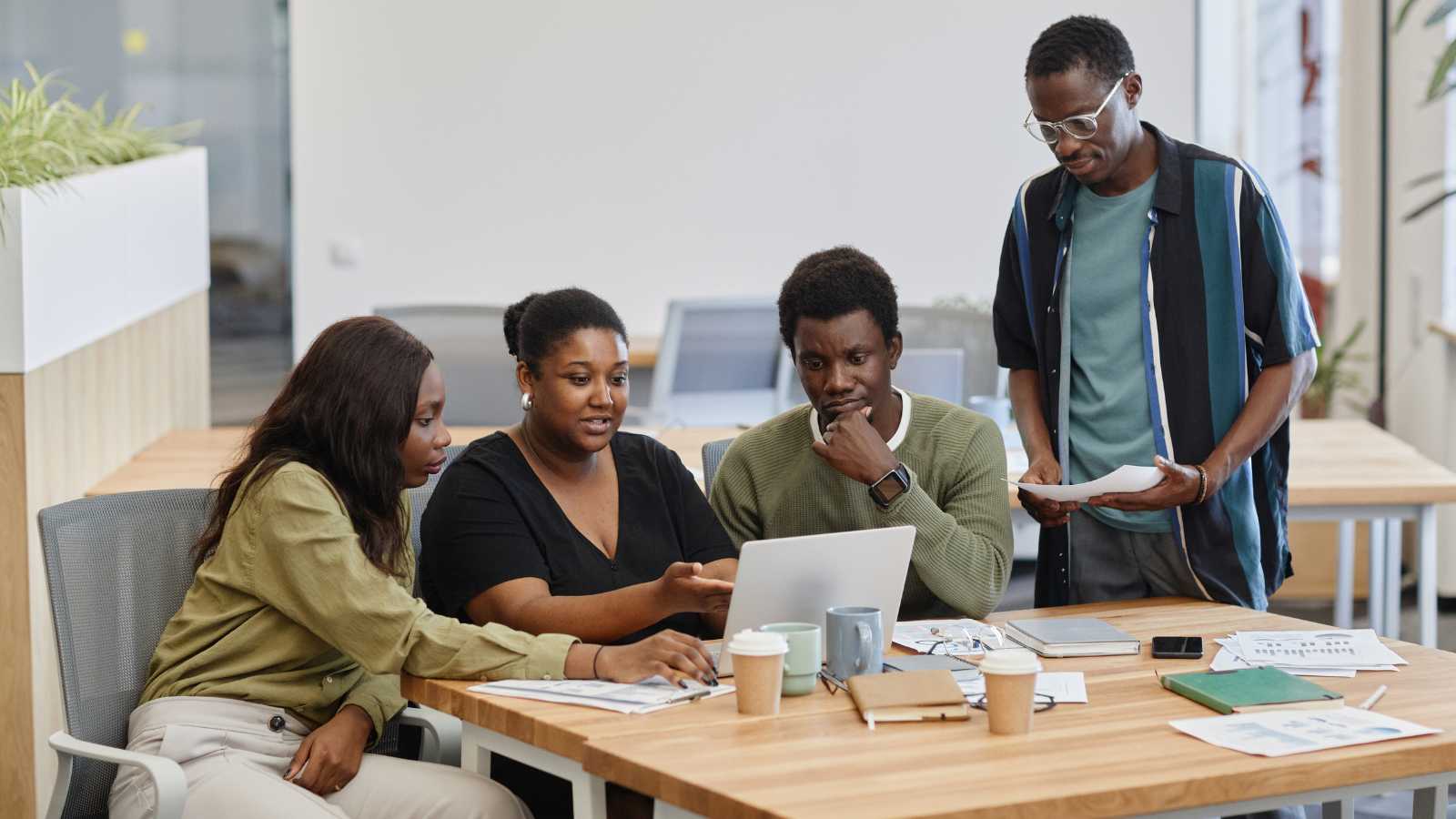 Four persons of African descent gathered around a laptop having a collaborative discussion.