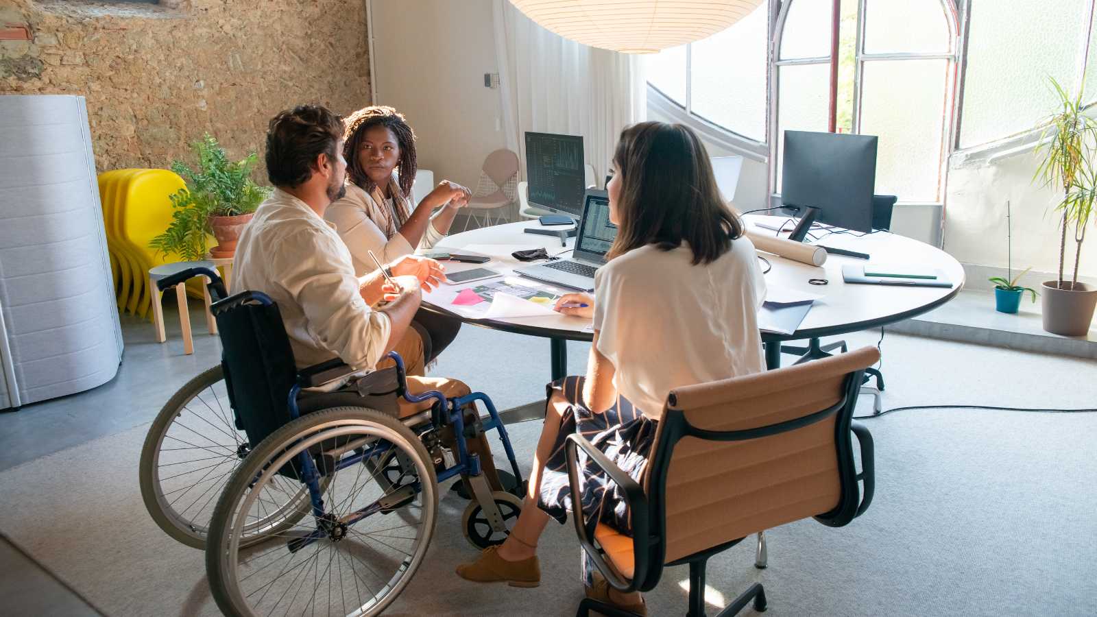 Three people sitting around a circle table, one in a wheel chair.