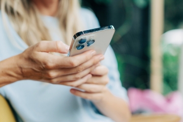 an image of a person in a seated position holding their smart phone in their right hand, supported by the left, interacting with the screen