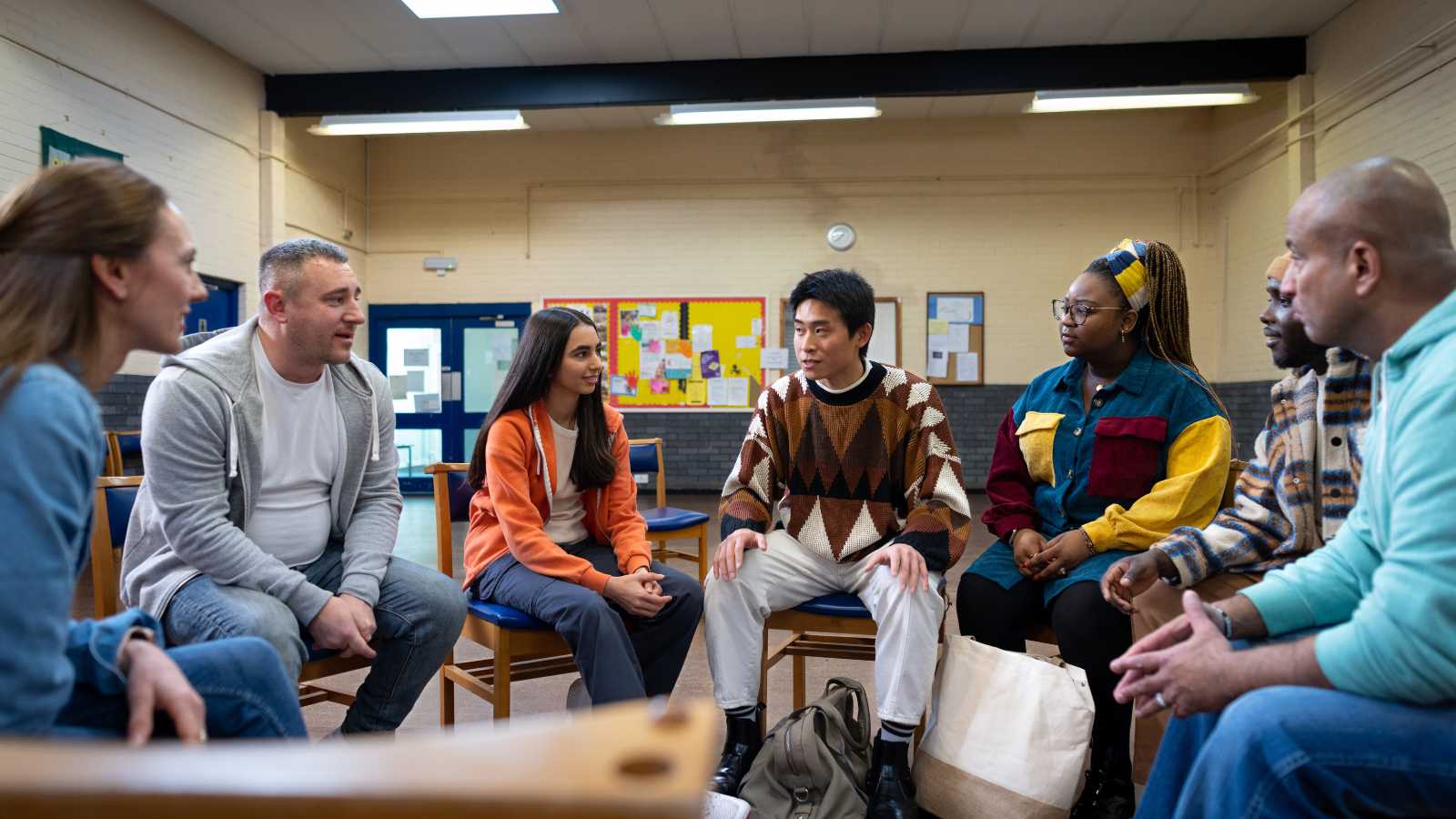 A group of people sitting in a room in a circle of chairs. 