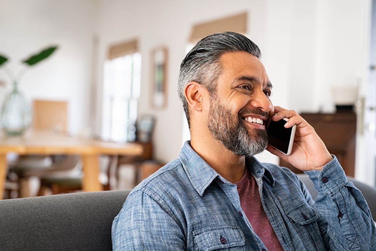 A man smiles while holding a smartphone up to his ear.