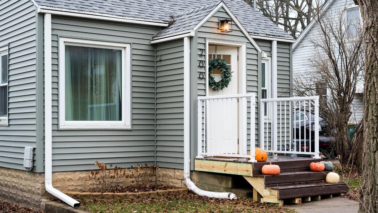 Front porch, white door, grey siding. Large bay window on left side. 