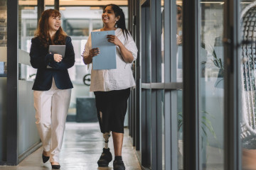 Two individuals, one with disabilities, walking side by side with documents in hands