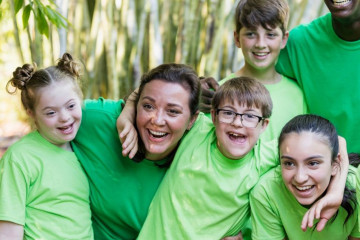 A group of six smiling people, two adults and four children, all wearing green shirts. There are trees in the background.