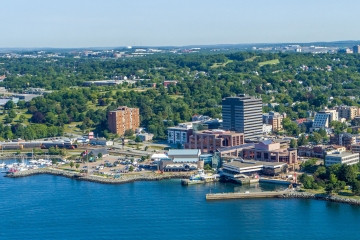 Aerial view of the Downtown Dartmouth waterfront featuring office buildings, the Alderney Landing complex and surrounding greenery along the shoreline. Text reads: "Planning & Development – Downtown Dartmouth Waterfront Revitalization Project. 