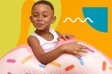 A photo of a young child with a sprinkle doughnut innertube in the foreground, with a bright orange background with colourful geometric shapes.
