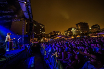 Two artists perform music on an outdoor stage in front of an audience.